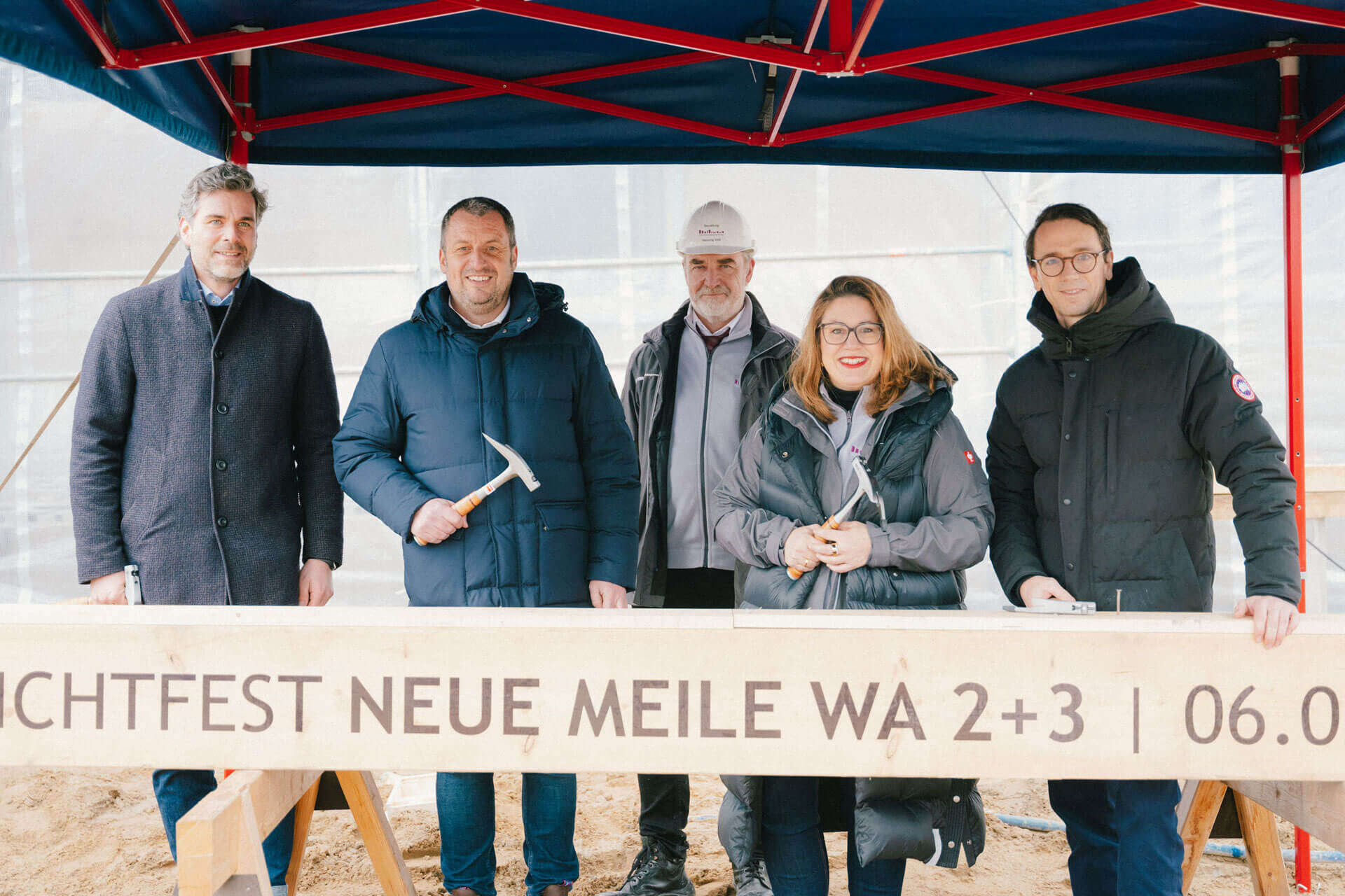 Richtfest in der Neuen Meile – Mehrere Beteilige hinter dem Banner Richtfest Neue Meile